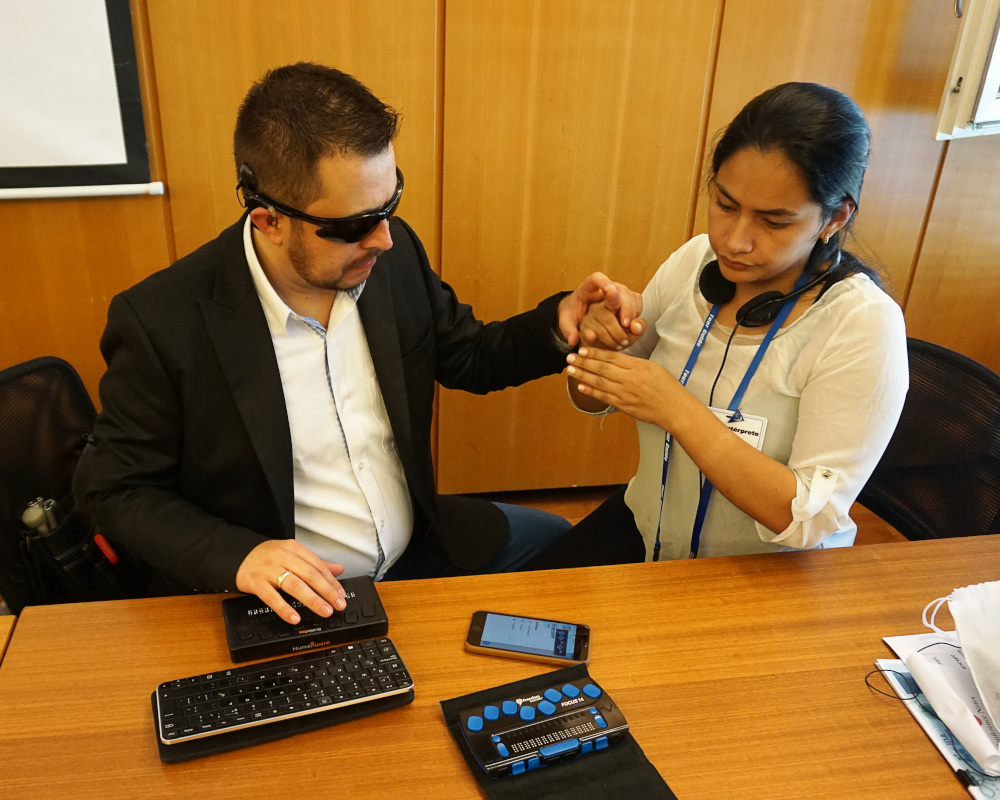 A participant using a braille line to navigate through his phone, with the assistance of an intepreter guide