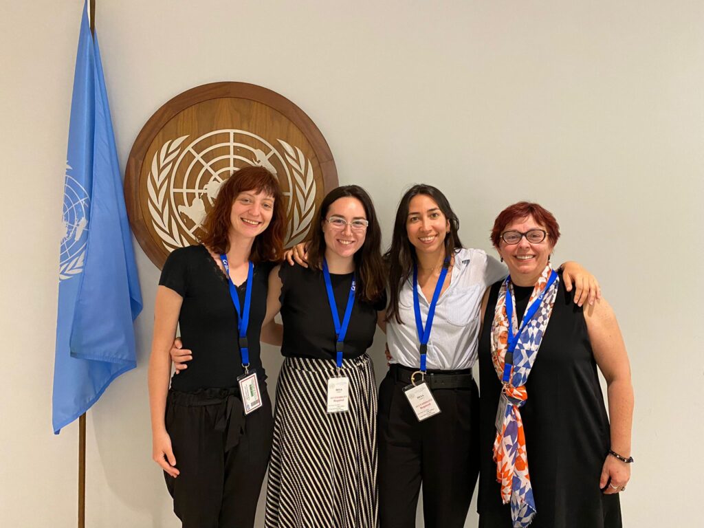 Four women smile at the camera by UN symbols