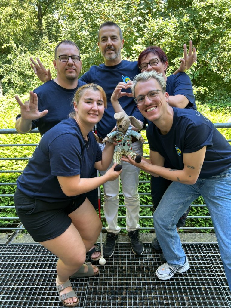 Five participants at the camp, including Frank and Sanja, pose playfully while holding a stuffed bunny. They are all wearing the same dark blue t-shirt.