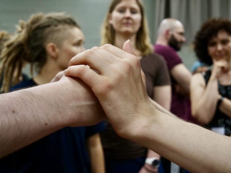 Two hands placed on top of each other, with a group of people visible in the background. Image courtesy of EDBY Camp.